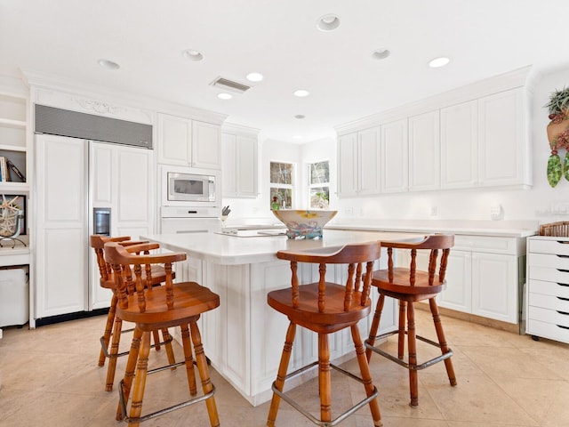 kitchen featuring white cabinets, built in appliances, light tile patterned floors, a kitchen island, and a breakfast bar area