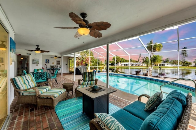 pool at dusk featuring a patio area, an outdoor living space, a water view, and glass enclosure