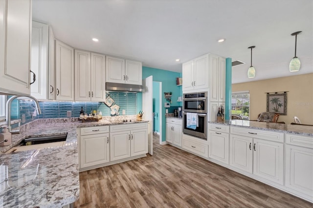 kitchen with decorative light fixtures, white cabinetry, double oven, and sink