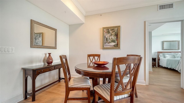 dining space featuring baseboards, visible vents, light wood finished floors, and ornamental molding