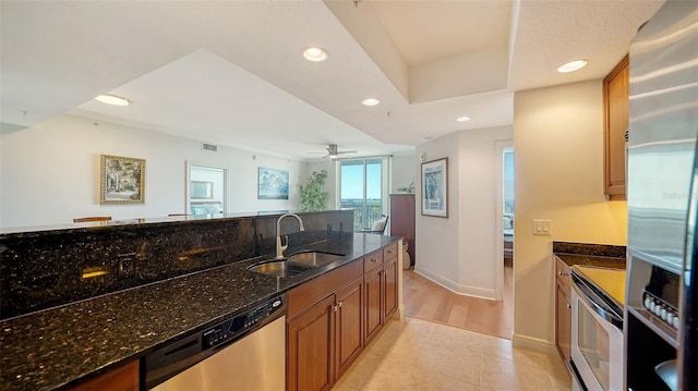 kitchen with dark stone countertops, brown cabinetry, recessed lighting, a sink, and appliances with stainless steel finishes