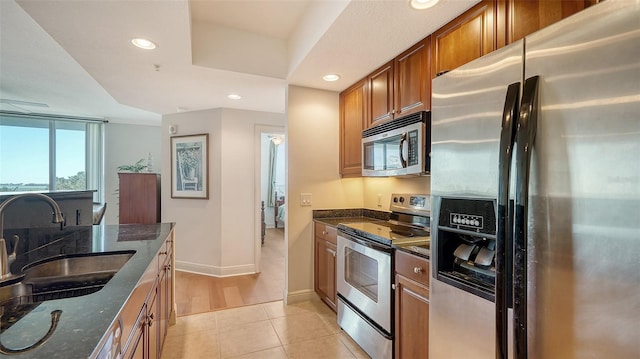 kitchen with dark stone counters, light tile patterned floors, brown cabinets, stainless steel appliances, and a sink