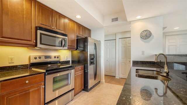 kitchen with a sink, dark stone counters, brown cabinets, and appliances with stainless steel finishes