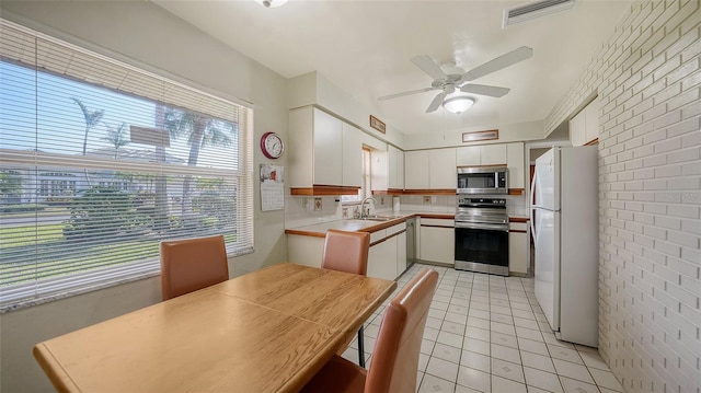 kitchen featuring appliances with stainless steel finishes, white cabinetry, and brick wall