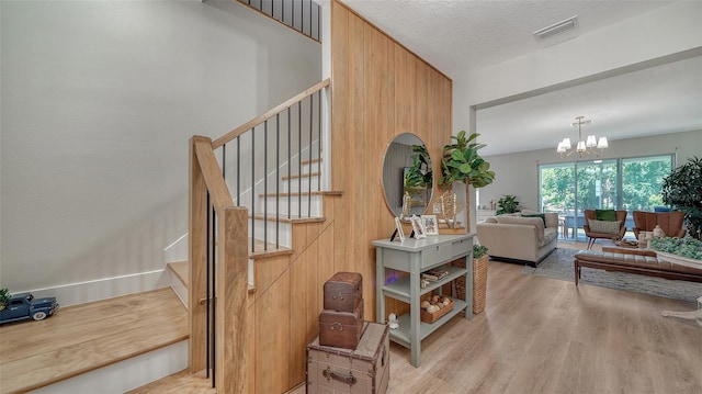 stairs with a textured ceiling, hardwood / wood-style flooring, and an inviting chandelier