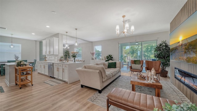 living room with a fireplace, a wealth of natural light, light hardwood / wood-style flooring, and an inviting chandelier