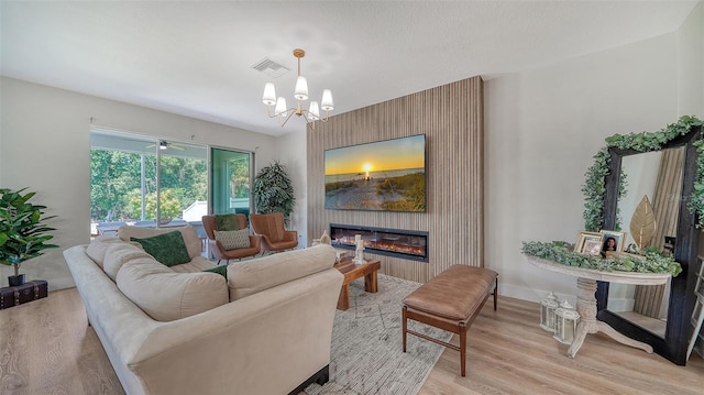 living room featuring a large fireplace, light hardwood / wood-style floors, and ceiling fan with notable chandelier