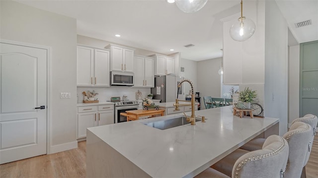 kitchen featuring sink, stainless steel appliances, light hardwood / wood-style floors, decorative light fixtures, and white cabinets