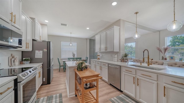 kitchen featuring white cabinets, appliances with stainless steel finishes, light wood-type flooring, and hanging light fixtures