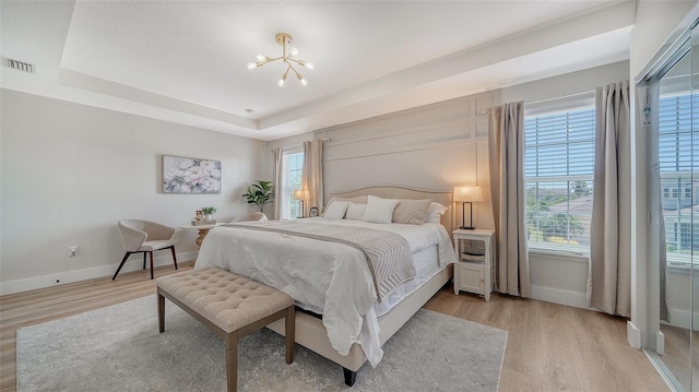 bedroom with a tray ceiling, multiple windows, and light wood-type flooring