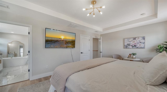 bedroom featuring an inviting chandelier, light hardwood / wood-style flooring, ensuite bath, and a tray ceiling