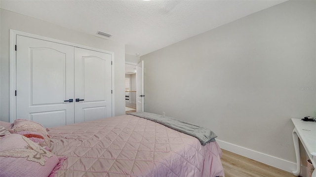 bedroom with a closet, a textured ceiling, and light hardwood / wood-style flooring