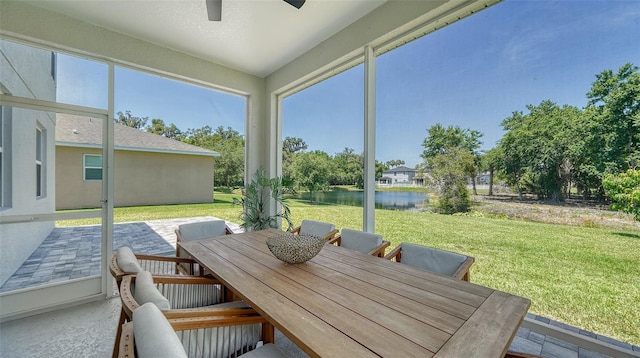 sunroom with ceiling fan and a water view