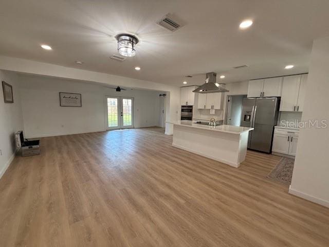 kitchen featuring stainless steel refrigerator with ice dispenser, ventilation hood, a kitchen island with sink, french doors, and white cabinets