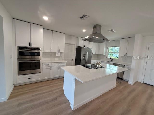 kitchen with exhaust hood, white cabinetry, a center island with sink, stainless steel appliances, and decorative backsplash