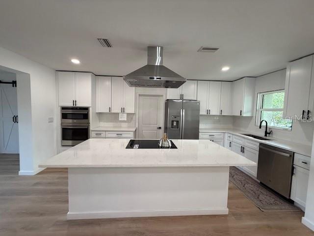 kitchen with wall chimney range hood, a center island, sink, white cabinetry, and stainless steel appliances