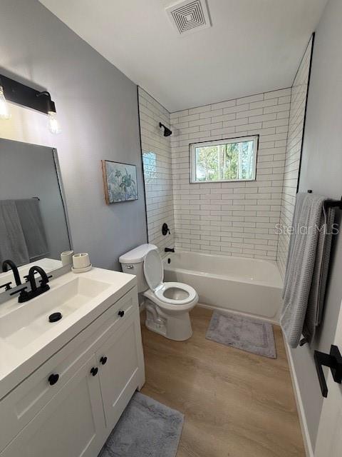 full bathroom with toilet, tiled shower / bath, vanity, and hardwood / wood-style floors