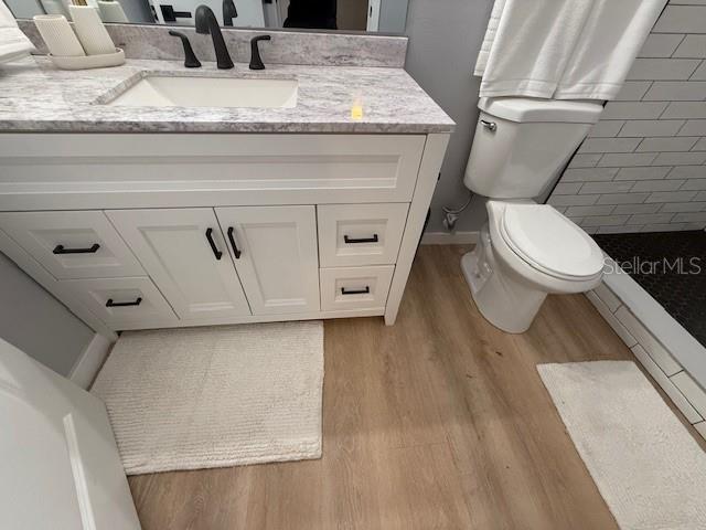 bathroom with hardwood / wood-style flooring, a shower, toilet, and vanity