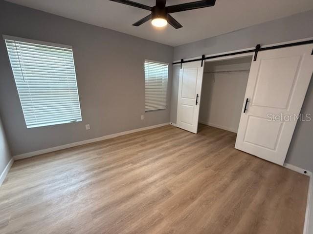 unfurnished bedroom featuring ceiling fan, light hardwood / wood-style floors, a closet, and a barn door