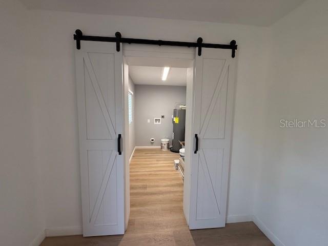 corridor with electric water heater, light hardwood / wood-style flooring, and a barn door