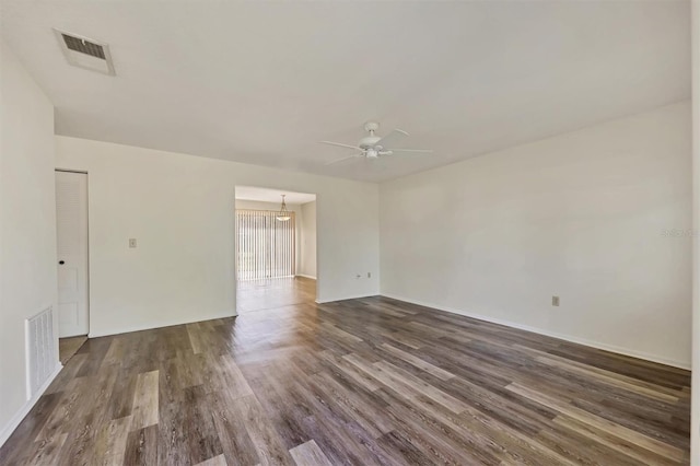 spare room with ceiling fan with notable chandelier and dark wood-type flooring