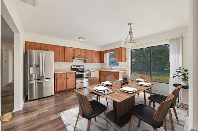 kitchen with appliances with stainless steel finishes, hanging light fixtures, dark wood-type flooring, and sink