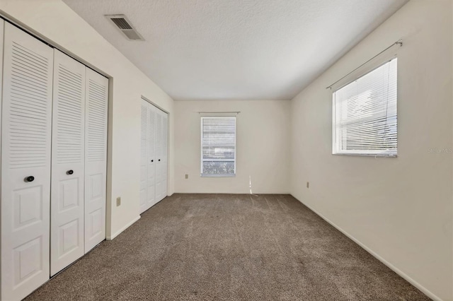 unfurnished bedroom featuring carpet, a textured ceiling, multiple windows, and multiple closets