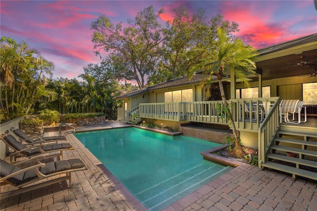 pool at dusk featuring ceiling fan, a patio area, and a deck