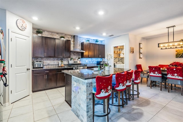 kitchen featuring washing machine and clothes dryer, wall chimney range hood, stainless steel range oven, pendant lighting, and a breakfast bar