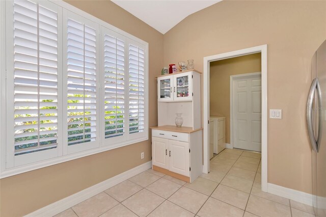 kitchen featuring lofted ceiling, white cabinetry, washing machine and dryer, and light tile patterned floors