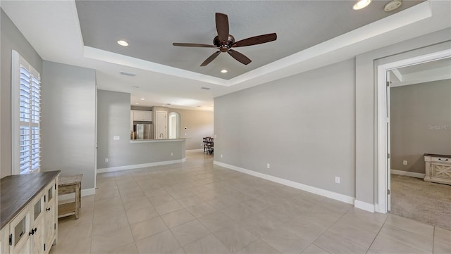 unfurnished living room featuring ceiling fan and a raised ceiling