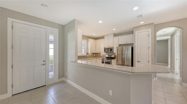 kitchen featuring kitchen peninsula, appliances with stainless steel finishes, backsplash, light tile patterned floors, and white cabinets