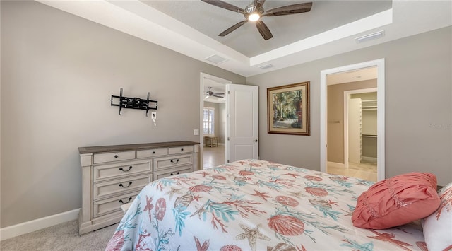 bedroom featuring light carpet, a tray ceiling, a spacious closet, and ceiling fan