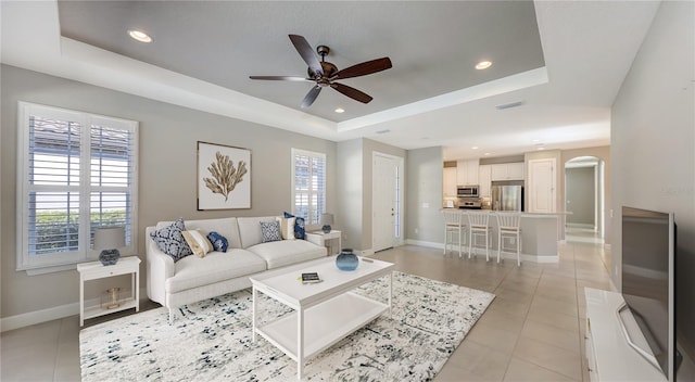 living room with a tray ceiling, ceiling fan, light tile patterned floors, and a healthy amount of sunlight