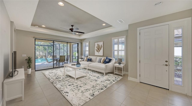 living room featuring a tray ceiling, ceiling fan, and light tile patterned floors