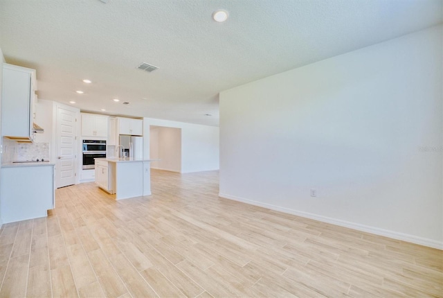 kitchen with white cabinetry, an island with sink, light hardwood / wood-style floors, decorative backsplash, and appliances with stainless steel finishes