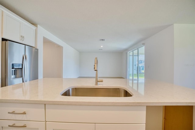 kitchen featuring light stone countertops, sink, stainless steel fridge with ice dispenser, white cabinetry, and an island with sink