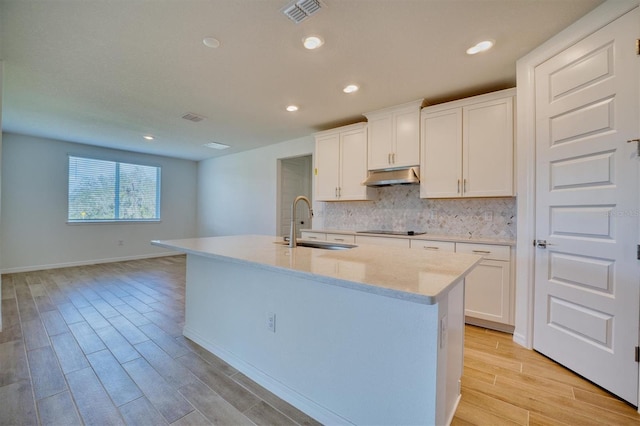 kitchen with sink, light hardwood / wood-style flooring, white cabinetry, and an island with sink