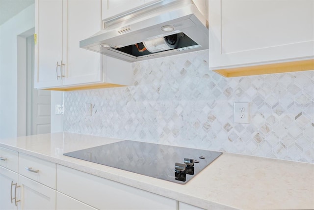 kitchen with black electric cooktop, light stone counters, white cabinets, and exhaust hood