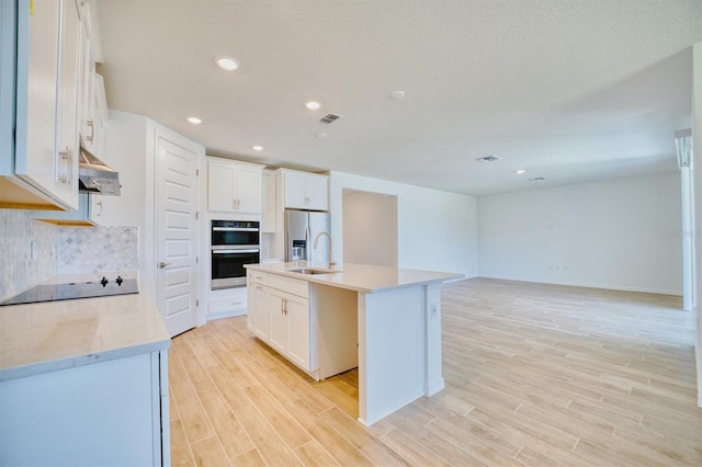 kitchen with appliances with stainless steel finishes, light wood-type flooring, sink, white cabinets, and an island with sink