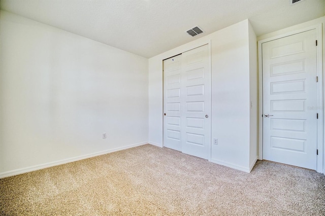 unfurnished bedroom featuring a textured ceiling, light colored carpet, and a closet