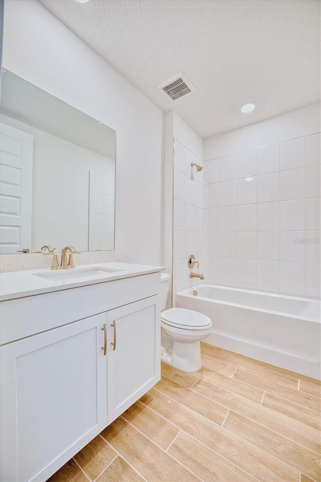 full bathroom with wood-type flooring, a textured ceiling, toilet, vanity, and tiled shower / bath