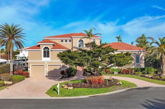 mediterranean / spanish home featuring a tile roof, decorative driveway, an attached garage, and stucco siding