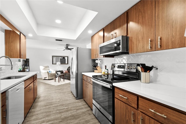 kitchen featuring sink, stainless steel appliances, a raised ceiling, backsplash, and light hardwood / wood-style floors