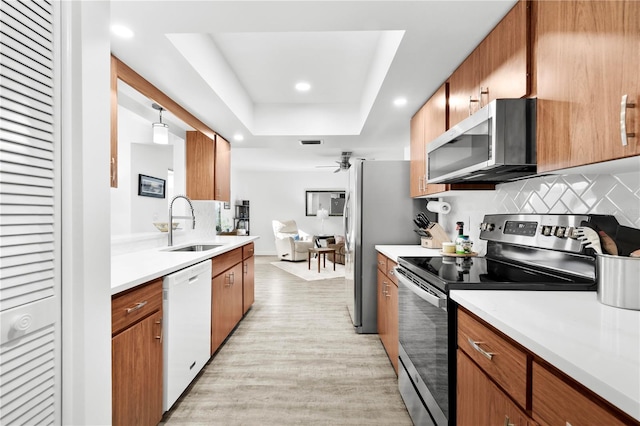 kitchen featuring a raised ceiling, sink, stainless steel appliances, and light hardwood / wood-style floors