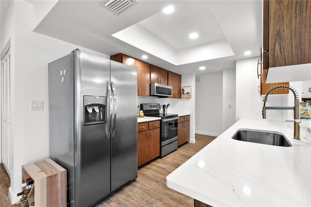 kitchen with light wood-type flooring, stainless steel appliances, a tray ceiling, and sink