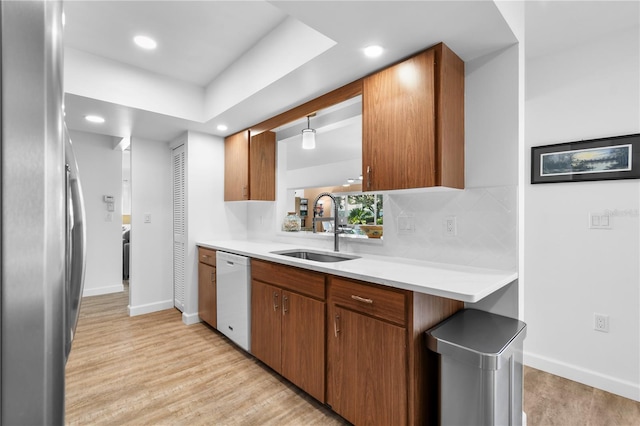 kitchen featuring stainless steel refrigerator, dishwasher, sink, hanging light fixtures, and light hardwood / wood-style flooring