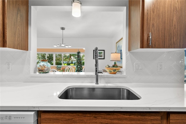 kitchen featuring light stone countertops, sink, hanging light fixtures, backsplash, and white dishwasher