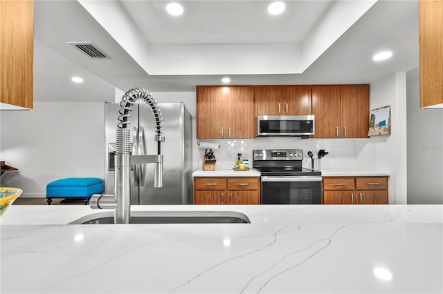 kitchen with light stone countertops, stainless steel appliances, tasteful backsplash, and a tray ceiling