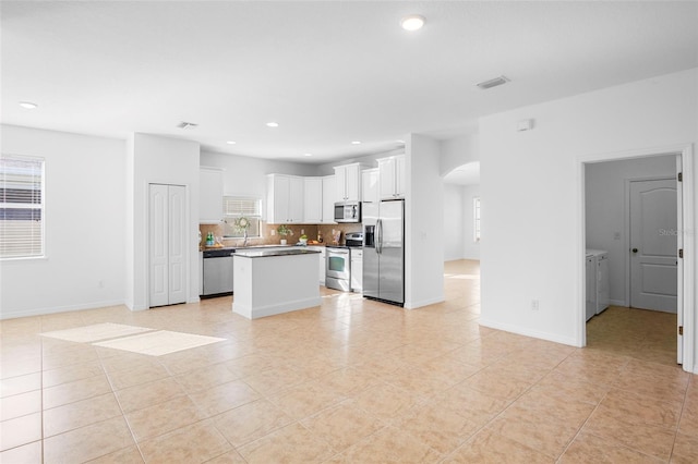 kitchen with washing machine and dryer, stainless steel appliances, a center island, white cabinets, and decorative backsplash